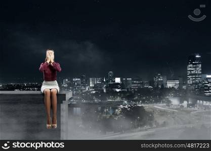 Depressed woman. Young woman sitting on building top and covering face with palms