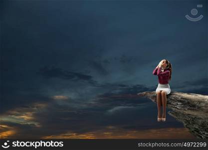Depressed woman. Young woman sitting on rock top and covering face with palms