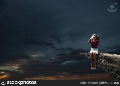 Depressed woman. Young woman sitting on rock top and covering face with palms