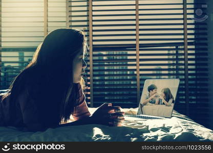 depressed Women sitting and looking Happy Asian Lover on the bed via technology laptop on the bed in the dark bedroom with low light environment,dramatic concept