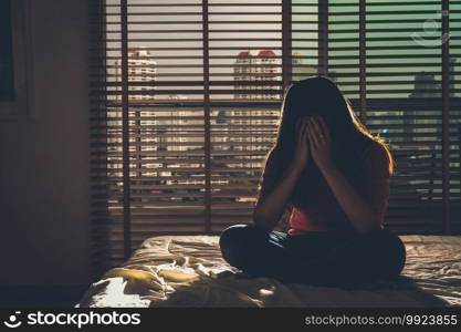 depressed Women sitting head in hands on the bed in the dark bedroom with low light environment, dramatic concept