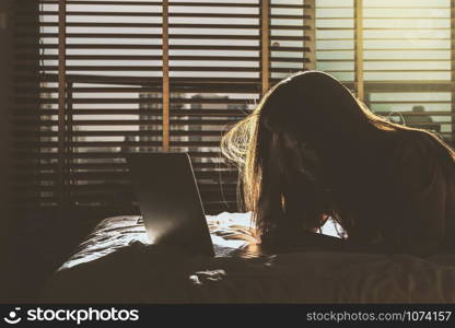 depressed Women sitting head in hands when working with technology laptop on the bed in the dark bedroom with low light environment, dramatic concept