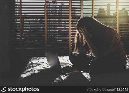 depressed Women sitting head in hands when working with technology laptop on the bed in the dark bedroom with low light environment, dramatic concept