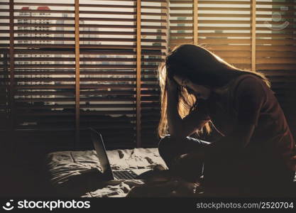 depressed Women sitting head in hands when working with technology laptop on the bed in the dark bedroom with low light environment, dramatic concept