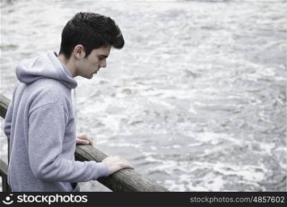 Depressed Young Man Contemplating Suicide On Bridge Over River
