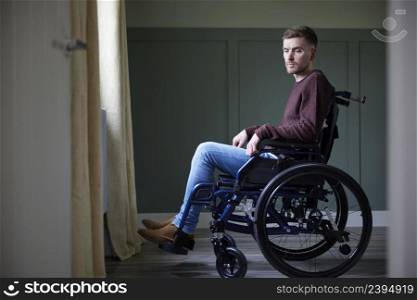 Depressed Young Man With Poor Mental Health In Wheelchair By Window At Home