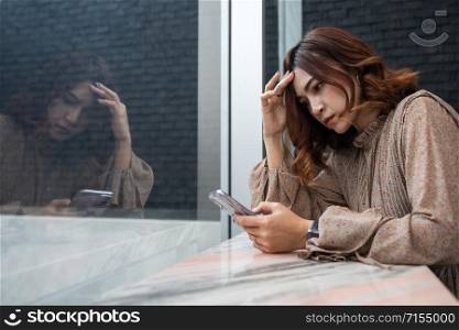 depressed young woman looking at her smartphone and having headache, feeling sad, worry about problem