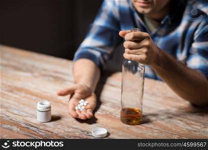 depression, drug abuse and addiction people concept - unhappy drunk man with bottle of alcohol and pills committing suicide by overdosing on medication at night. unhappy drunk man with bottle of alcohol and pills