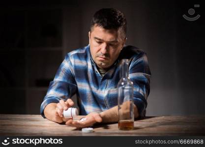 depression, drug abuse and addiction people concept - unhappy drunk man with bottle of alcohol and pills committing suicide by overdosing on medication at night. unhappy drunk man with bottle of alcohol and pills. unhappy drunk man with bottle of alcohol and pills