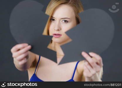 Depression, sadness, relationship problem concept. Young female with broken heart full of negative sad emotions. Woman covering her face by two parts of black love symbol.. Young sad woman covered by broken heart.