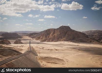 Desert landscape with blue sky and sun with road,sand and mountains