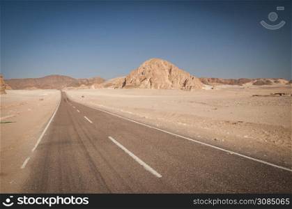 Desert landscape with blue sky and sun with road, sand and mountains