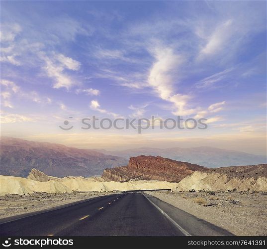 Desert road leading through Death Valley National Park at sunset , California USA.