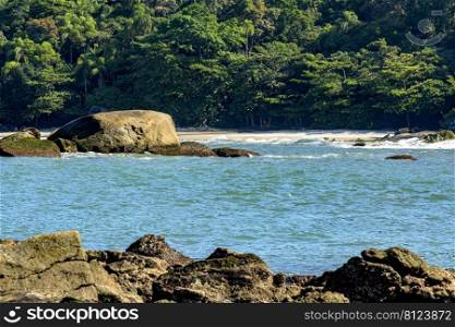 Deserted beach with colorful and transparent waters between the rocks, mountains and tropical forests of Bertioga on the coast of Sao Paulo, Brazil. Deserted beach with colorful and transparent waters between the rocks, mountains and rainforest