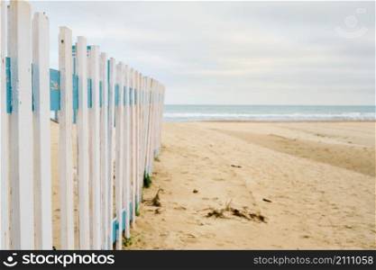 Deserted spring beach, fence in front of a public beach, cloudy sky in anticipation of rain. Off-season sea beach, place for text
