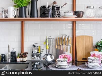 Design of a modern home kitchen in the loft-style. White wall with shelves, trays, jars, mugs, sink. In the background a wall of white brick
