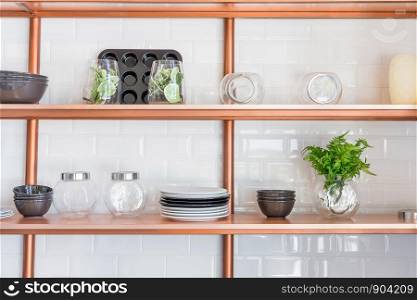 Design of a modern home kitchen in the loft-style. White wall with shelves, trays, jars, mugs, sink. In the background a wall of white brick