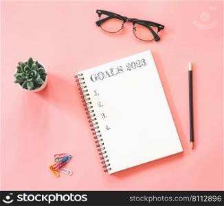 Design of workspace desk with blank notebook, with empty goals for 2023 year and phone on color background