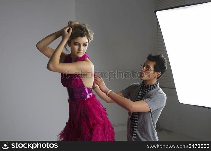 Designer adjusting dress back of fashion model in studio
