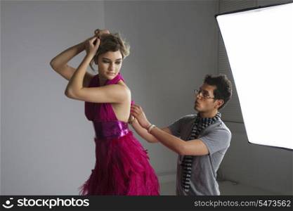 Designer adjusting dress back of fashion model in studio