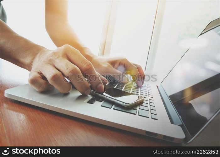 designer hand working and smart phone and laptop on wooden desk in office