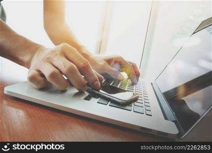 designer hand working and smart phone and laptop on wooden desk in office