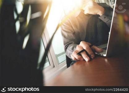 designer hand working laptop with green plant foreground on wooden desk in office