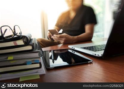 designer hand working with digital tablet and laptop and notebook stack and eye glass on wooden desk in office