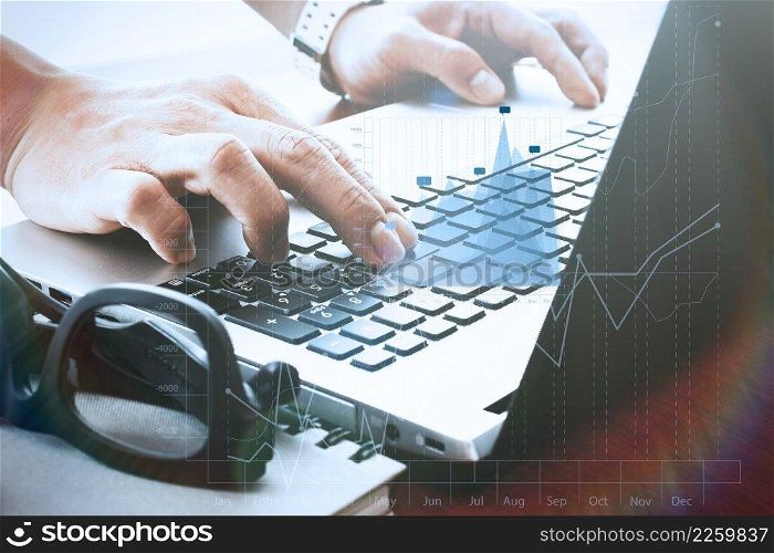 designer hand working with digital tablet and laptop and notebook stack and eye glass on wooden desk in office with business graph diagram
