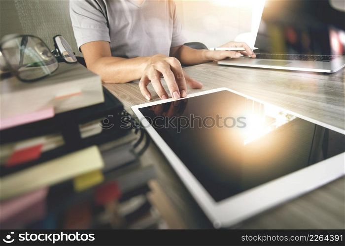 designer hand working with digital tablet and laptop and notebook stack and eye glass on wooden desk in office
