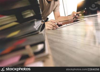 designer hand working with digital tablet and laptop computer and book stack on wooden desk as concept