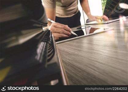 designer hand working with digital tablet and laptop computer and book stack  on wooden desk as concept