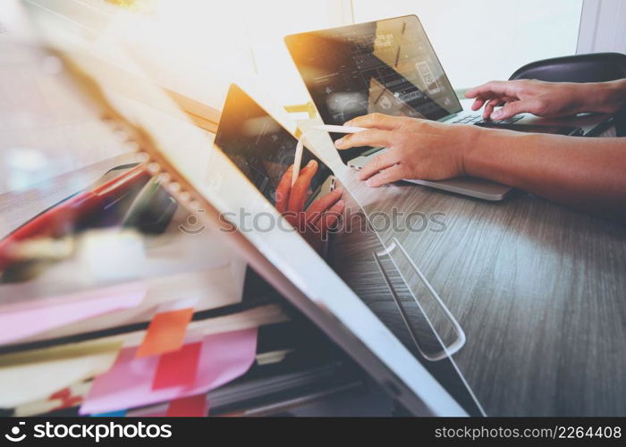 designer hand working with digital tablet and laptop computer and book stack and eye glass on wooden desk as concept