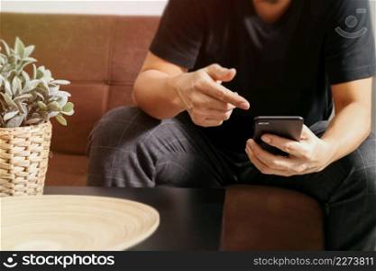 designer man hand using smart phon for mobile payments online shopping,omni channel,sitting on sofa in living room,vase rattan with plant and wooden tray on table
