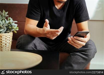 designer man hand using smart phon for mobile payments online shopping,omni channel,sitting on sofa in living room,vase rattan with plant and wooden tray on table