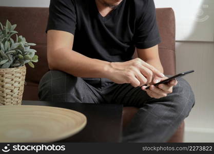 designer man hand using smart phon for mobile payments online shopping,omni channel,sitting on sofa in living room,vase rattan with plant and wooden tray on table