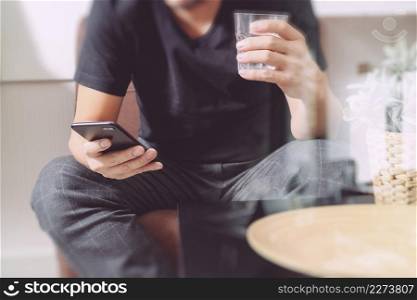 designer man hand with glass of water using smart phon for mobile payments online shopping,omni channel,sitting on sofa in living room,vase rattan with plant and wooden tray on table,filter