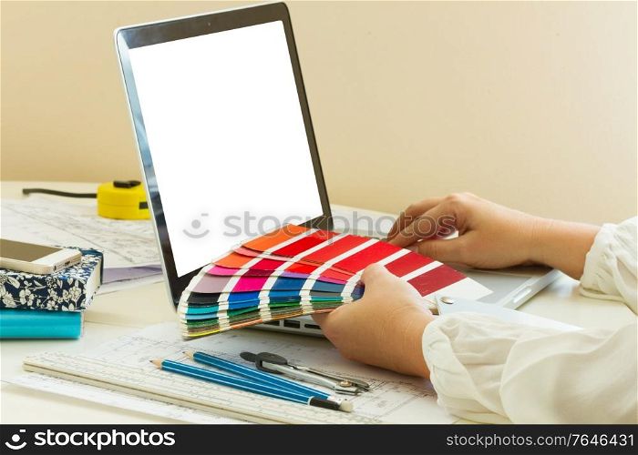 designer&rsquo;s working table - dhands of esigner holding colour charts, copy space on emptyy screen. designer&rsquo;s working table