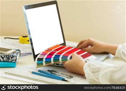 designer&rsquo;s working table - dhands of esigner holding colour charts, copy space on emptyy screen. designer&rsquo;s working table