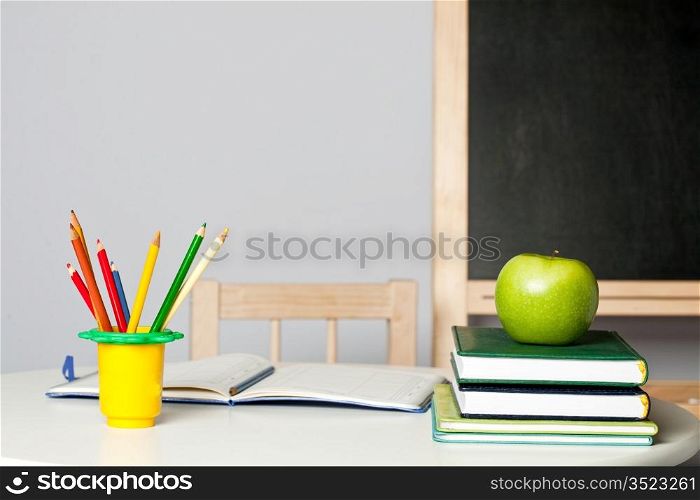 Desk with apple, pencil, notebook and textbook in class. School concept
