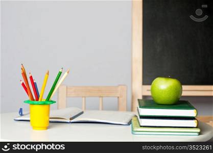 Desk with apple, pencil, notebook and textbook in class. School concept