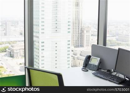 Desktop computer and landline phone on desk by glass window in office