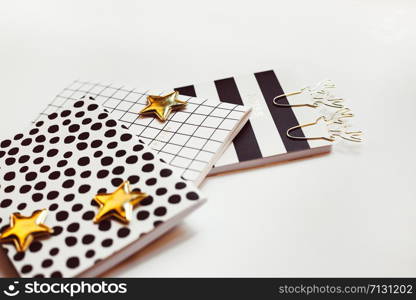 Desktop feminine composition with patterned notepads, golden stars and deer clips on white table with sun light and shadows. Close up concept for blogger