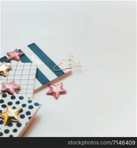 Desktop feminine composition with patterned notepads, golden stars and deer clips on white table with sun light and shadows. Toned Close up concept for blogger