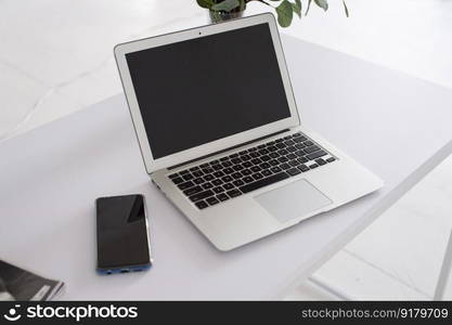 Desktop, smartphone, gadgets, office work, remote work, online, white room. Laptop on a white table next to the phone