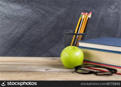 Desktop with reading materials and green apple in front of blackboard. Layout in horizontal format with copy space.