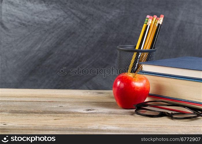 Desktop with reading materials and red apple in front of blackboard. Layout in horizontal format with copy space.