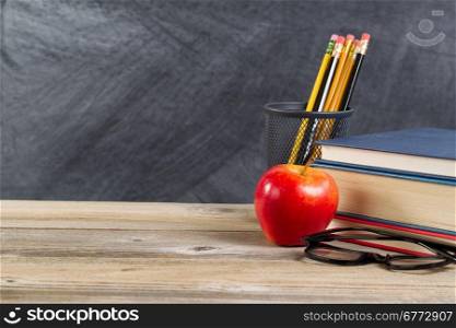 Desktop with reading materials and red apple in front of blackboard. Layout in horizontal format with copy space.
