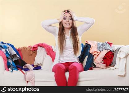 Desperate helpless woman in messy room home.. Desperate helpless woman sitting on sofa couch in messy living room with hands on head. Young girl surrounded by many stack of clothes. Disorder and mess at home.