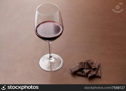 dessert concept - dark chocolate pieces and glass of red wine on brown background. dark chocolate pieces and glass of red wine